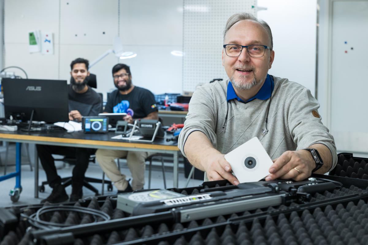 Laatupäällikkö Janne Väistöllä on käsissään Ecoaimis optisen ammunnan harjoittelupaketti. Tuotekehityksessä ohjelmointityötä tekevät Mahmudul Hasan (va) ja Zahid Abdullah.