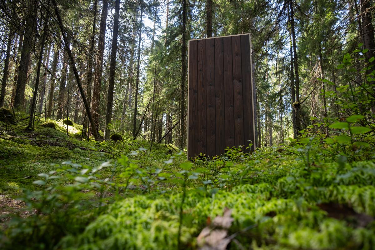 Metsässä ruskea puinen ovi, joka on tehty hiilletystä puusta.