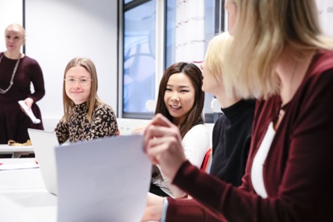 Studenter vid ett skrivbord med bärbara datorer och papper.