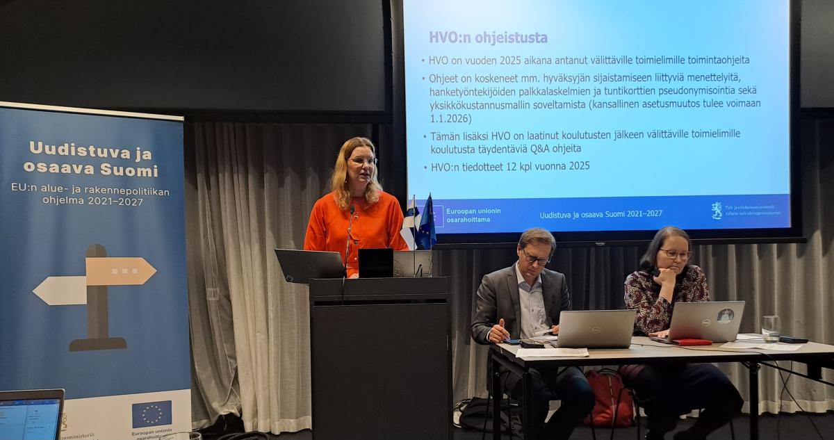 Kuvassa Petra Metsälä puhujanpöntön takana pitämässä esitystä. Pöntön vieressä pöytä, jonka takana istuvat Valtteri Karhu ja Johanna Osenius.