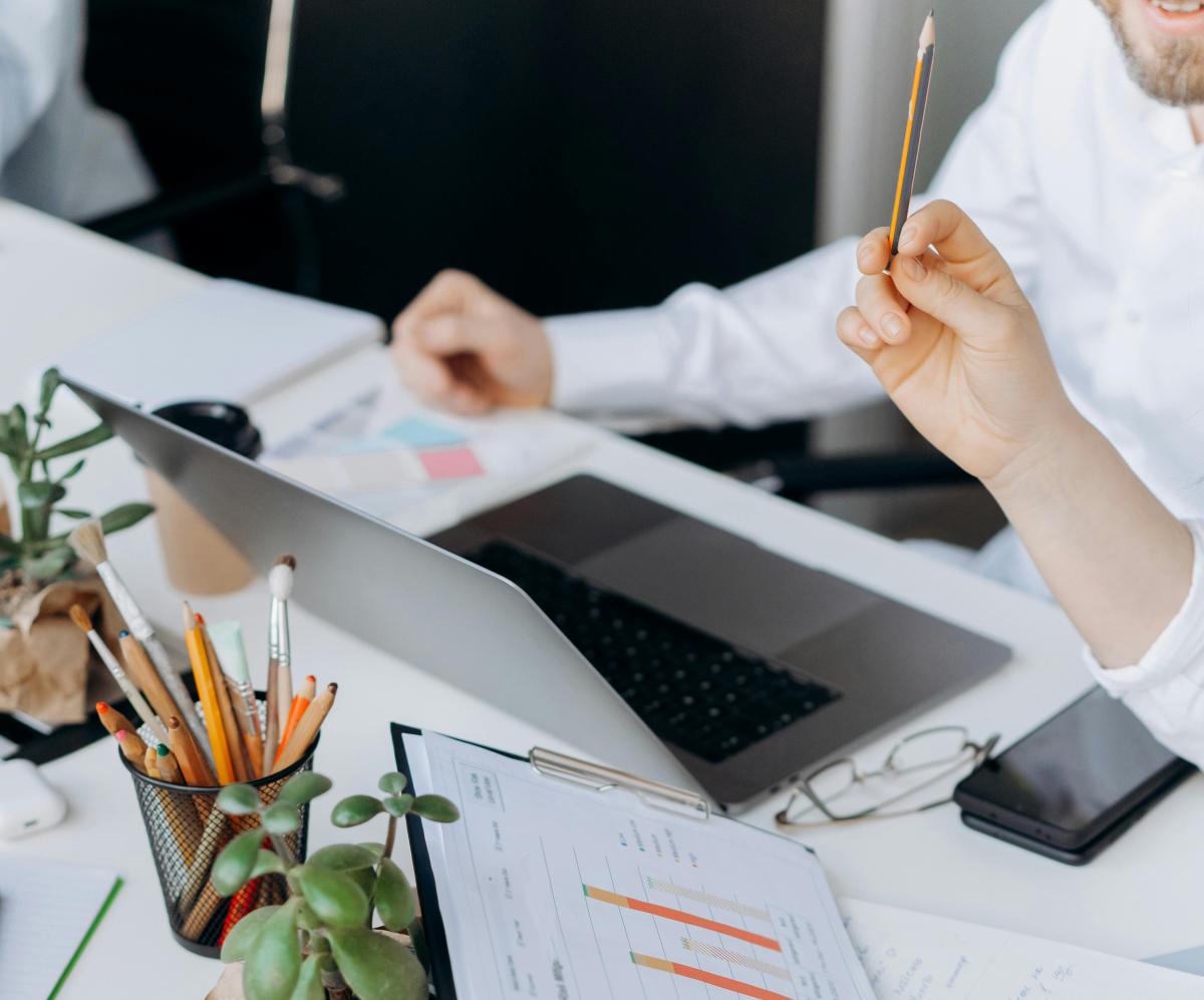 Toimistossa työpöytä, läppärin vieressä tilastopapereita ja ihmisiä tekemässä yhteistyötä.