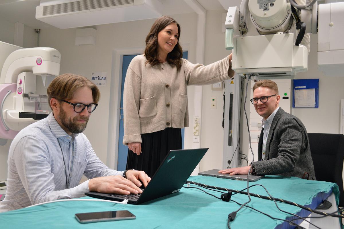 Yliopettaja Karoliina Paalimäki-Paakki ja professori, ylifyysikko Miika Nieminen esittelevät, miten Mittlab-laboratorion laitetta käytetään esimerkiksi murtuneen käden kuvantamiseksi. Sairaalafyysikko Timo Liimatainen seuraa vieressä suoritusta omalta koneeltaan.